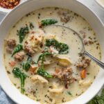 Bowl of creamy sausage tortellini soup garnished with red pepper and fresh grated Parmesan cheese.