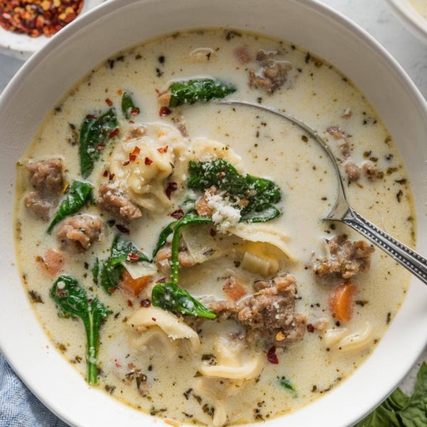 Bowl of creamy sausage tortellini soup garnished with red pepper and fresh grated Parmesan cheese.
