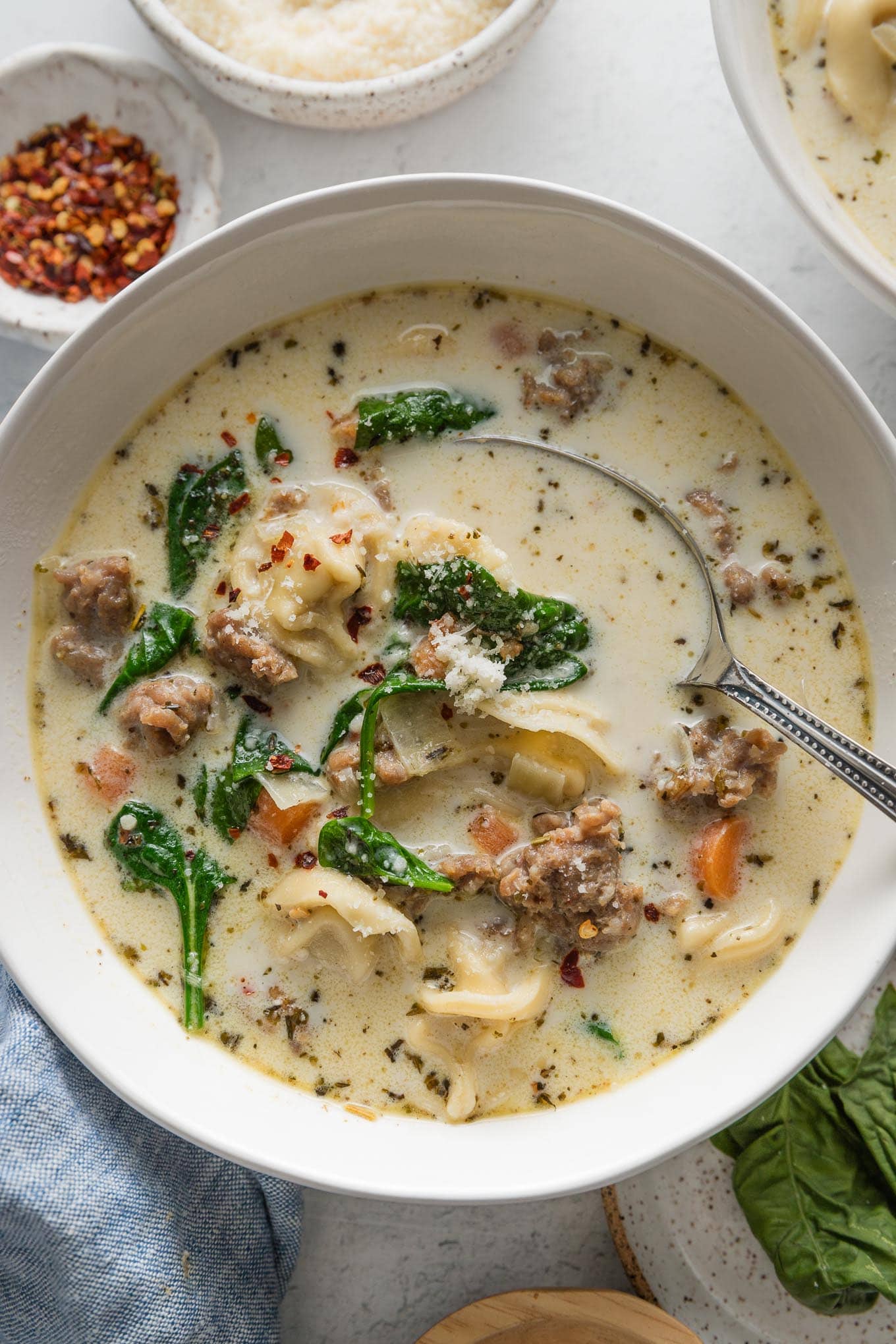 Bowl of creamy sausage tortellini soup garnished with red pepper and fresh grated Parmesan cheese.