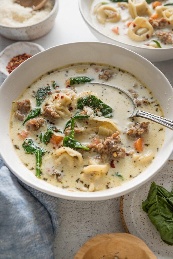 Angled view of a spoon lifting a bite of creamy sausage tortellini soup out of a small ceramic bowl.