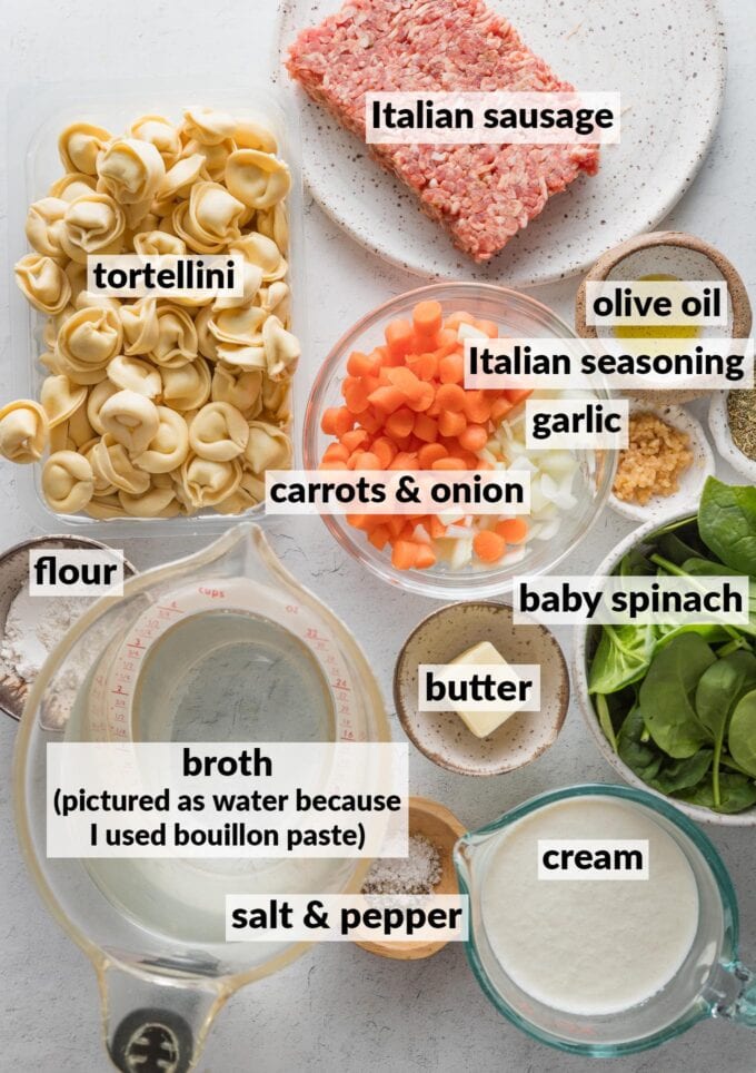 Labeled overhead photo of ingredients for a tortellini soup with sausage: fresh cheese tortellini, ground Italian sausage, broth, cream, chopped carrots and onions, Italian seasoning, minced garlic, butter and all-purpose flour, baby spinach, salt, and pepper.