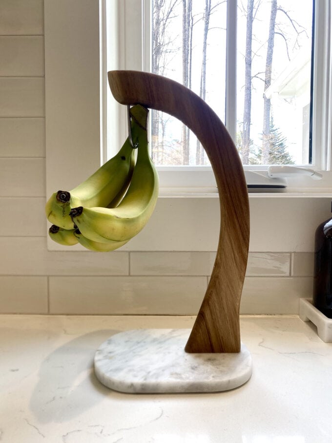 Banana hanger with several yellow bananas resting on a kitchen counter.