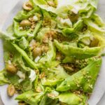 Close up of a white platter filled with a butter lettuce salad with Manchego cheese and Castelvetrano olives.