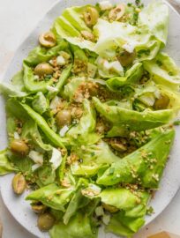 Close up of a white platter filled with a butter lettuce salad with Manchego cheese and Castelvetrano olives.