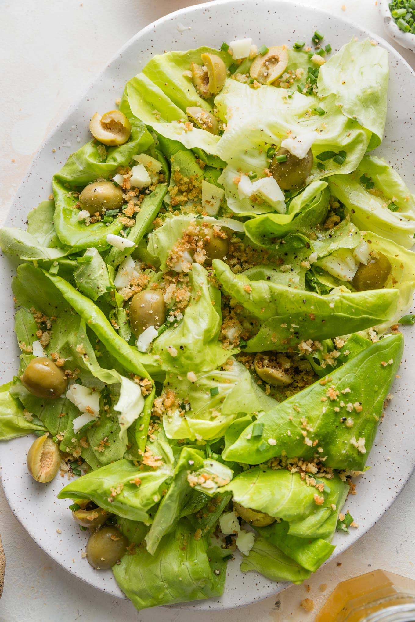 Close up of a white platter filled with a butter lettuce salad with Manchego cheese and Castelvetrano olives.