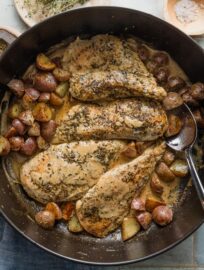 Overhead view of a large cast iron skillet filled with pan-fried chicken breasts and baby potatoes in a creamy Dijon mustard sauce.