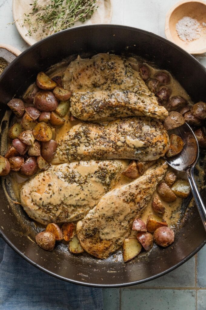 Overhead view of a large cast iron skillet filled with pan-fried chicken breasts and baby potatoes in a creamy Dijon mustard sauce.