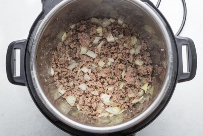 Ground beef, onion, and seasonings browned together in the inner pot of a 6-quart Instant Pot.