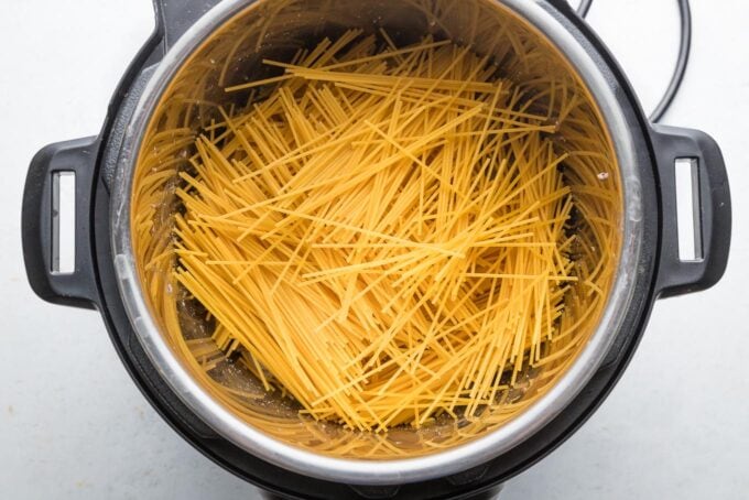 Dried spaghetti noodles layered on top of ground beef in a criss-cross pattern.