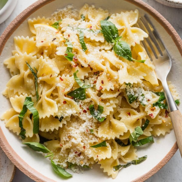Shallow bowl full of a simple basil pasta dish with a hint of lemon juice and Parmesan cheese.