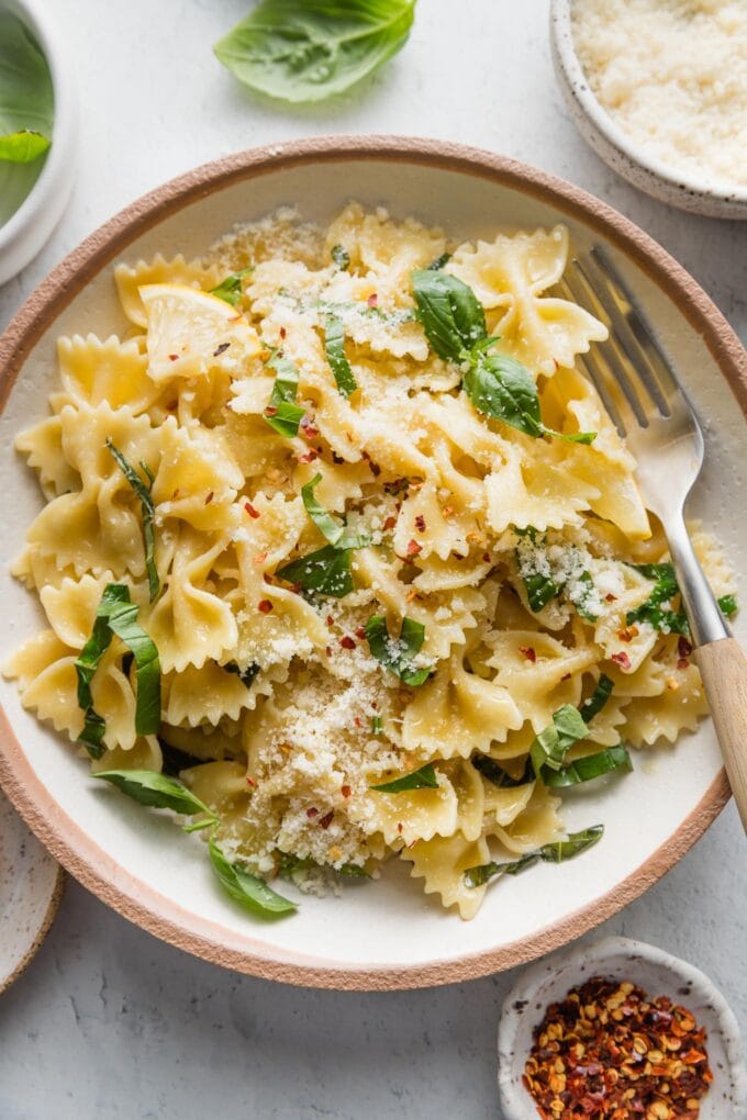 Shallow bowl full of a simple basil pasta dish with a hint of lemon juice and Parmesan cheese.
