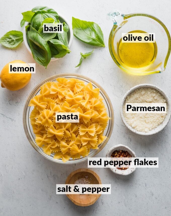 Labeled overhead image of dried bowtie pasta, olive oil, Parmesan, fresh basil, a whole lemon, red pepper flakes, salt and pepper.