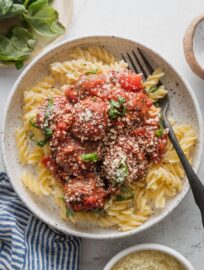 Small bowl of pasta with homemade meatballs in a quick but from scratch marinara sauce, served with slivers of basil and grated Parmesan.