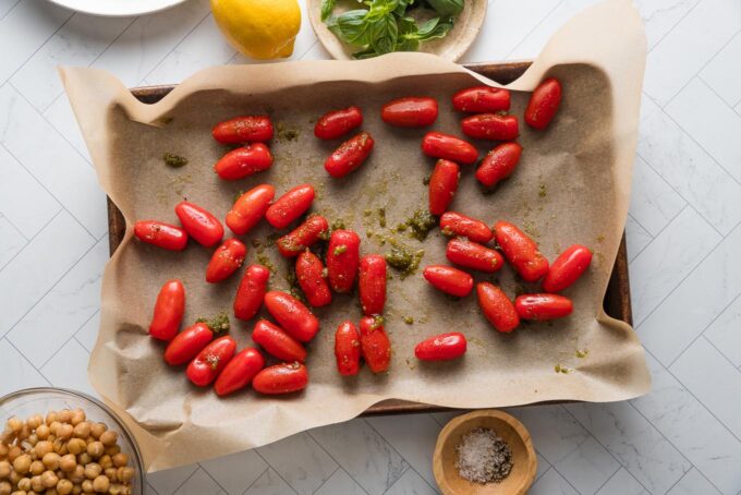 Cherry tomatoes tossed with pesto and spread out on a parchment-lined baking sheet.