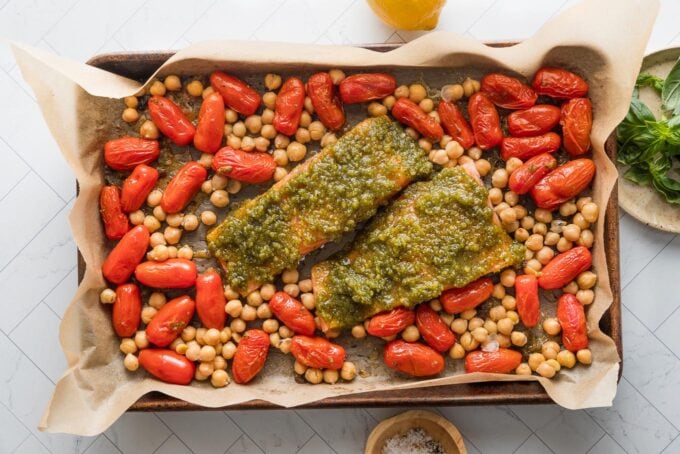Parchment lined sheet pan with cherry tomatoes, chickpeas, and salmon filets with pesto.