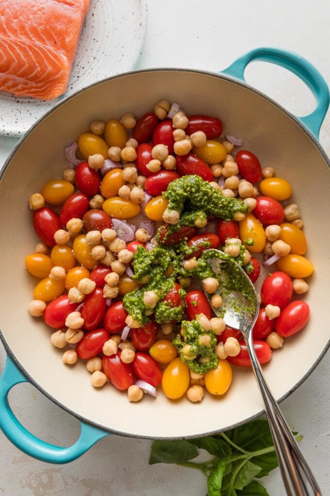 Pesto being stirred into tomato-chickpea mixture.