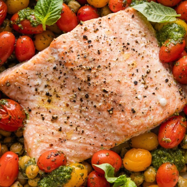 Close up of oven roasted salmon with pesto, tomatoes, chickpeas, and shallot in a shallow enameled roasting pan.