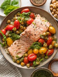 Bowl full of oven roasted salmon, cherry tomatoes, chickpeas, and shallot with basil pesto, served over pearl couscous.