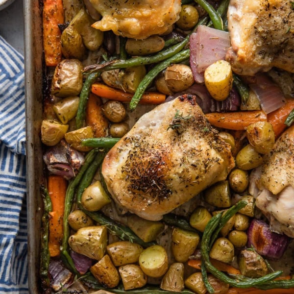 Overhead view of a large rimmed sheet pan with roasted chicken thighs and veggies seasoned with Herbes de Provence.