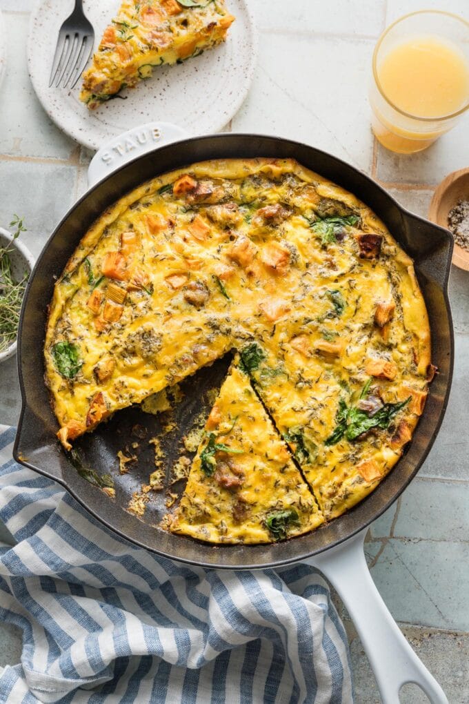 Overhead view of a sweet potato frittata with ground Italian sausage, cheese, and thyme, in a small cast iron skillet with one slice removed.