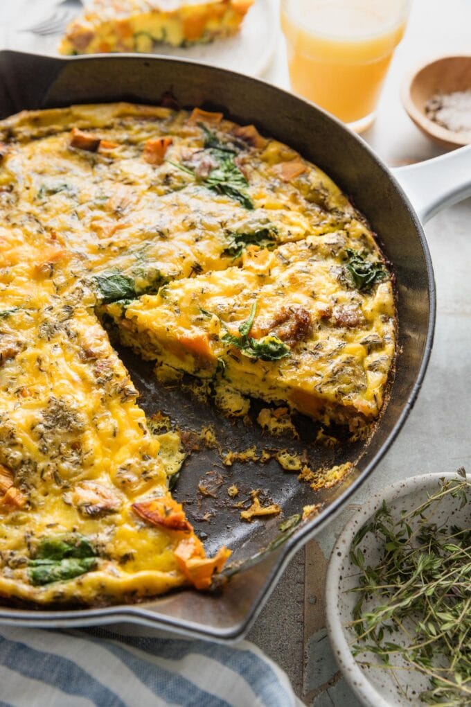 Angled view of a sliced frittata, still in the skillet, showing cubed sweet potato and browned sausage baked into the interior.