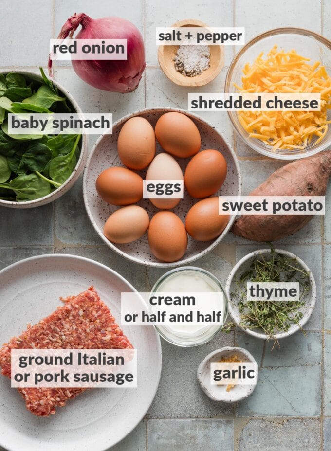 Labeled overhead photo of whole eggs, ground Italian sausage, baby spinach, fresh thyme, a red onion, a sweet potato, cheddar cheese, cream, salt, and pepper, all in prep bowls or ready to chop and prep for a meal.