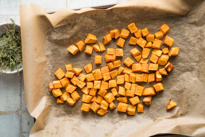 Cubed sweet potatoes roasted on a parchment-lined baking sheet.