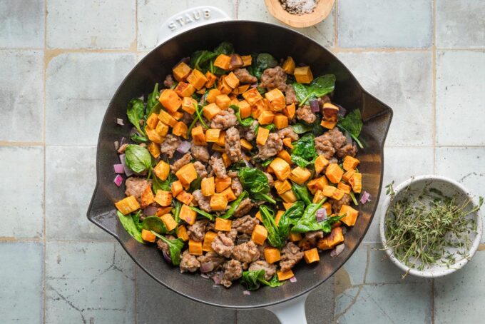 Sweet potato cubes added to sausage and spinach in a cast iron skillet.