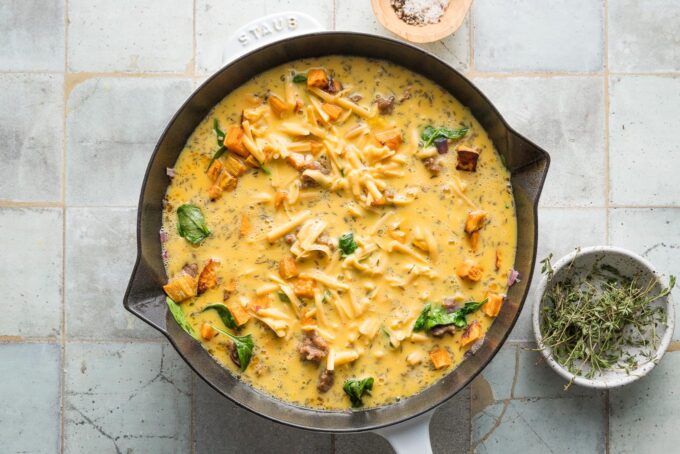 Egg-cream mixture poured over sweet potatoes and sausage in a skillet to bake into a frittata.