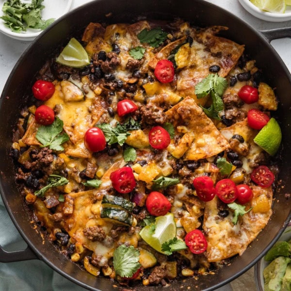 Overhead view of a deep cast iron skillet with an enchilada dish of ground beef, veggies, and tortillas all cooked together in enchilada sauce and spices.