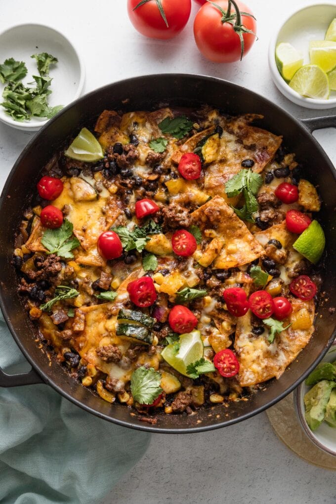 Overhead view of a deep cast iron skillet with an enchilada dish of ground beef, veggies, and tortillas all cooked together in enchilada sauce and spices.
