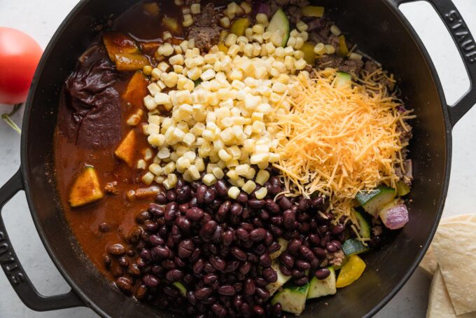 Cheese, corn, and beans added into an enchilada skillet.