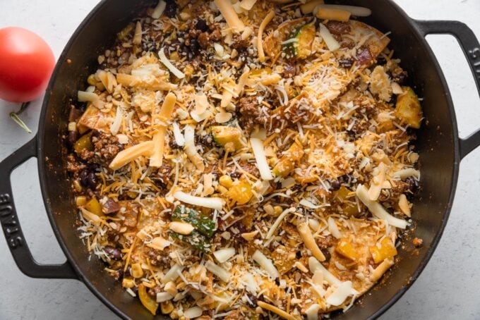 Shredded Mexican cheese sprinkled on top of an enchilada skillet.