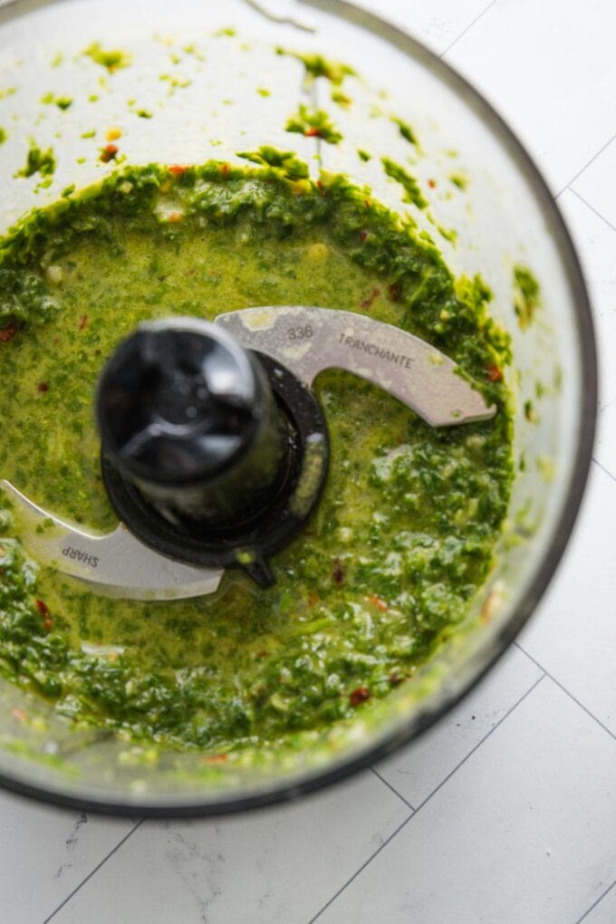 Close up homemade basil vinaigrette pulsed together in the bowl of a miniature food processor.