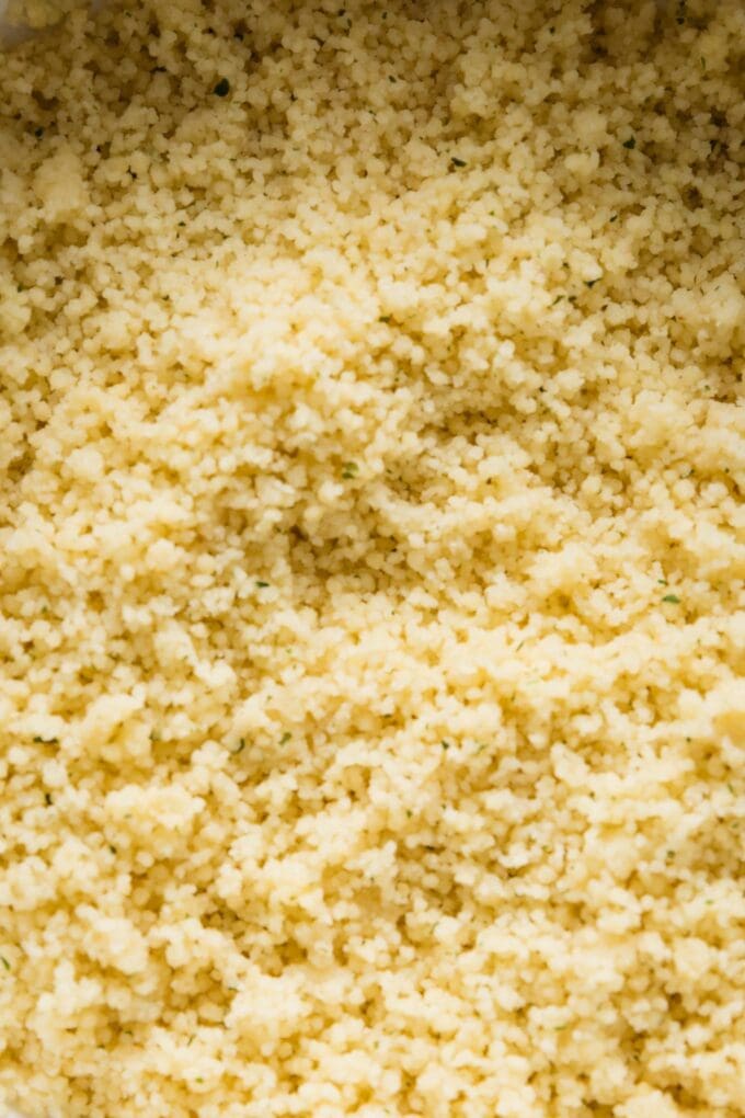 Close up of cooked couscous fluffed and transferred into a white ceramic salad bowl.