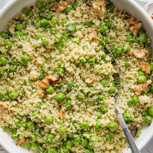 Bowl filled with a light, freshly-made couscous salad with peas, walnuts, and a homemade basil vinaigrette dressing.