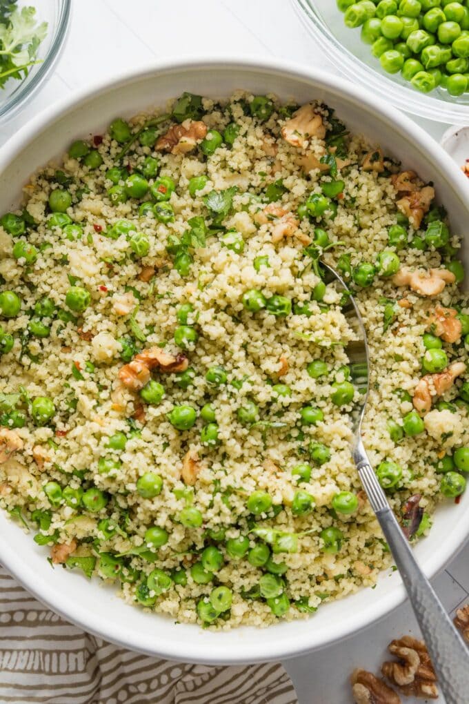 Bowl filled with a light, freshly-made couscous salad with peas, walnuts, and a homemade basil vinaigrette dressing.