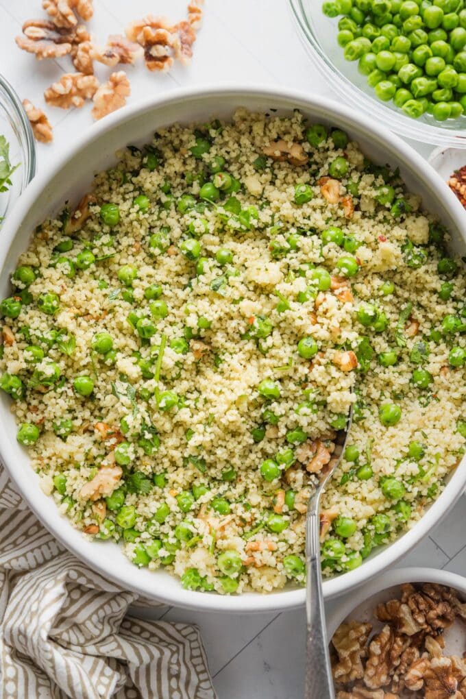 Countertop set with a large bowl full of a spring couscous salad packed with peas, walnuts, parsley, and an herb vinaigrette.
