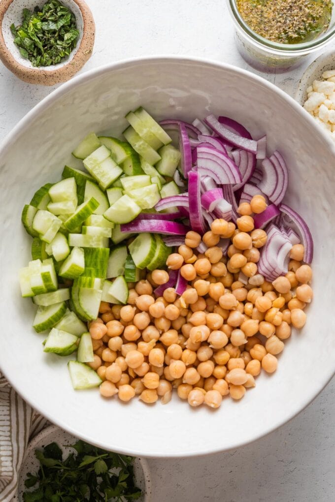 Bowl full of drained and rinsed chickpeas, chopped cucumber, and thinly-sliced red onion.
