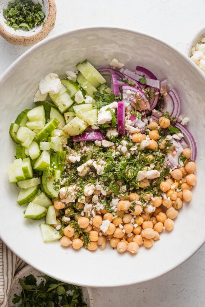 Chickpea and cucumber salad with fresh herbs and a light dressing poured on top, but not yet mixed in.