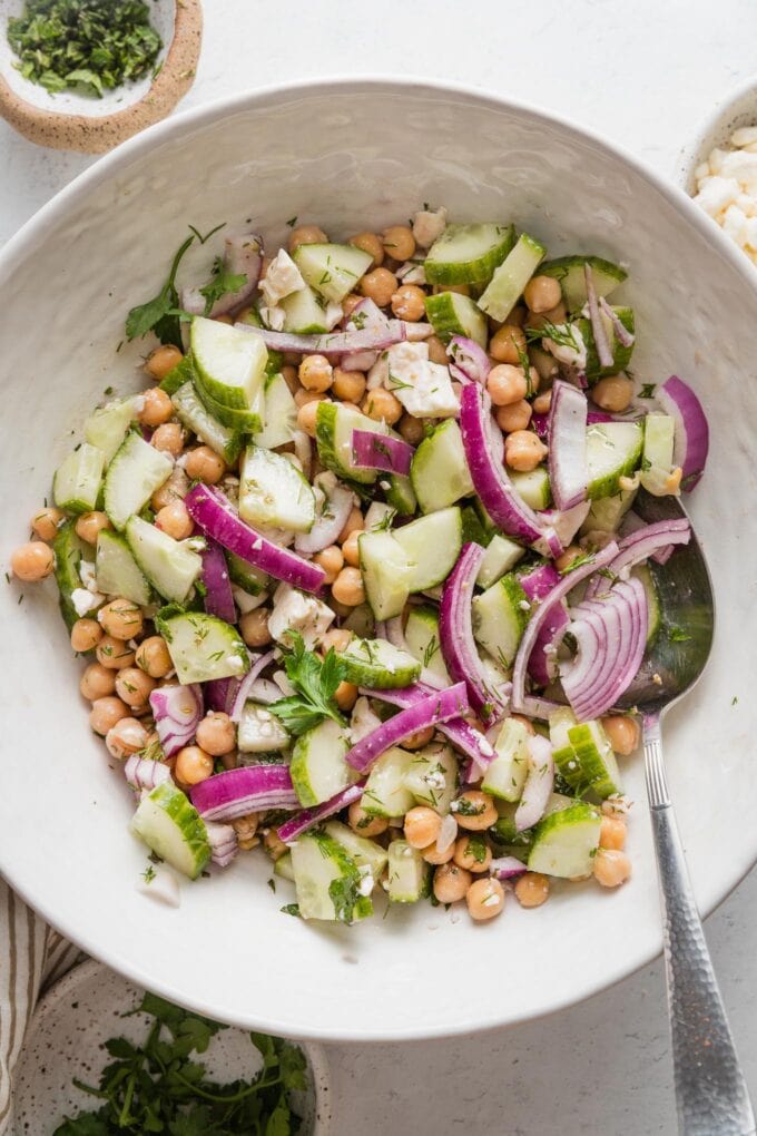 White bowl full of a simple cucumber chickpea salad with a homemade Greek-inspired dressing.