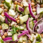 Close up of a chickpea cucumber salad with red onions, feta, fresh herbs, and a Greek-inspired vinaigrette dressing.