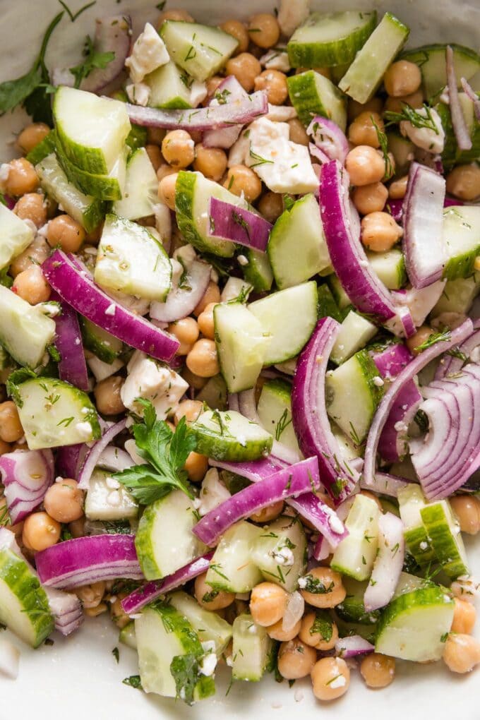 Close up of a chickpea cucumber salad with red onions, feta, fresh herbs, and a Greek-inspired vinaigrette dressing.