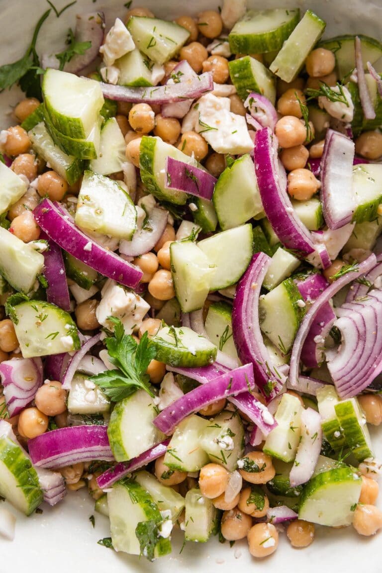 Close up of a chickpea cucumber salad with red onions, feta, fresh herbs, and a Greek-inspired vinaigrette dressing.