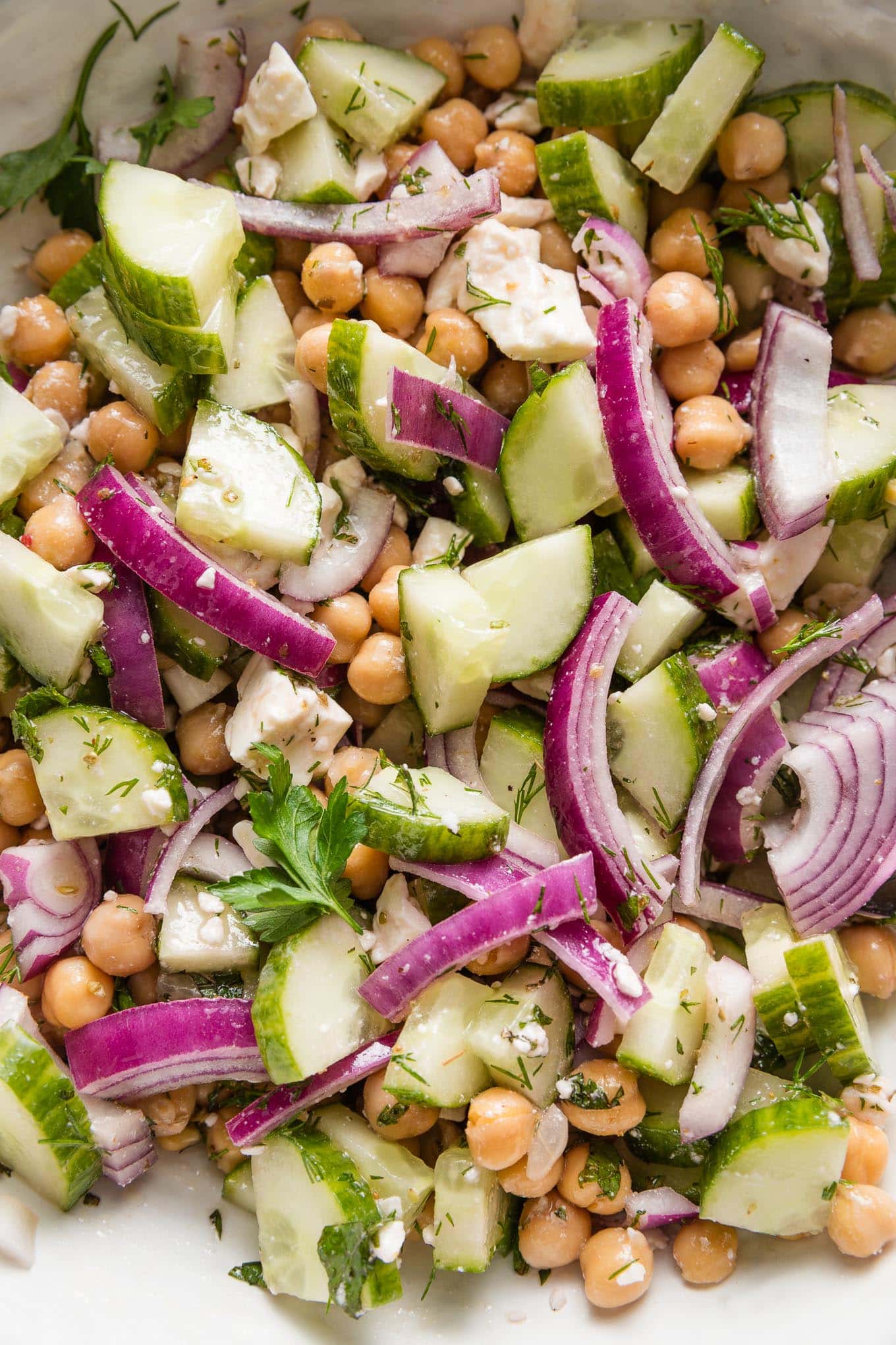 Close up of a chickpea cucumber salad with red onions, feta, fresh herbs, and a Greek-inspired vinaigrette dressing.