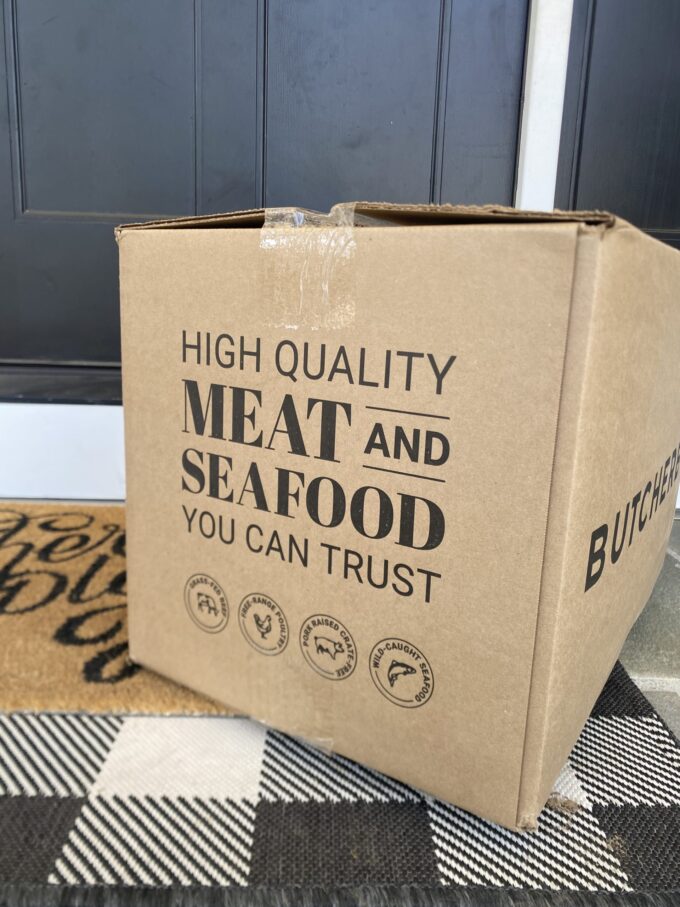 Angled view of an unopened ButcherBox with the slogan, "High quality meat and seafood you can trust" clearly visible.