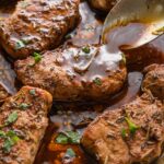 Close up of a spoon pouring balsamic pan sauce over seared pork medallions in the pan.