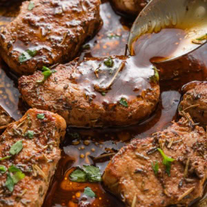 Close up of a spoon pouring balsamic pan sauce over seared pork medallions in the pan.