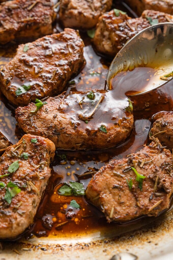 Close up of a spoon pouring balsamic pan sauce over seared pork medallions in the pan.