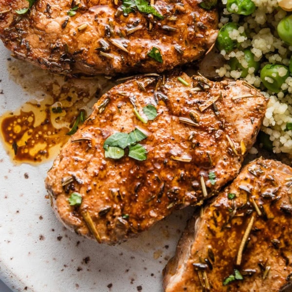 Close up of pork tenderloin medallions pan-seared in a simple homemade balsamic pan sauce, garnished with fresh parsley, and plated with a couscous and pea salad.